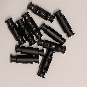 May include: A group of ten black plastic cord locks, also known as toggle stoppers, for adjusting the length of cords or straps.