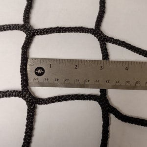 Pu&ograve; includere: Primo piano di una rete da carico nera con un righello che misura la dimensione della maglia. La maglia &egrave; larga circa 2,5 cm.