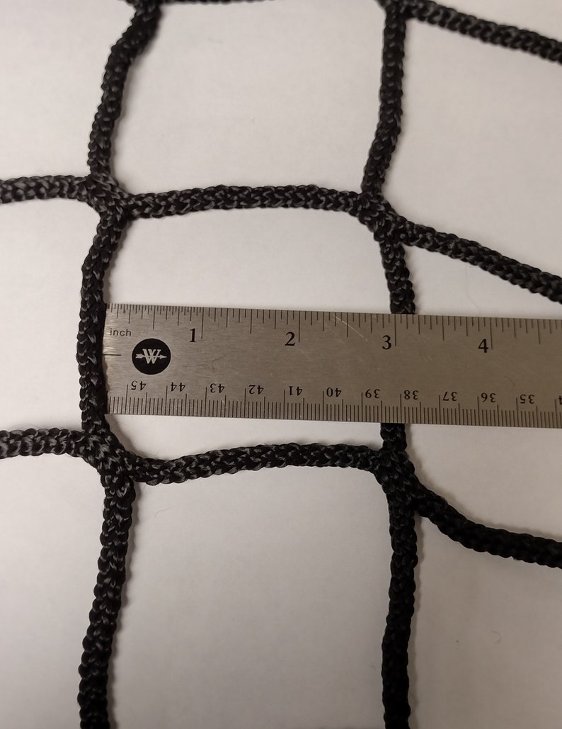 Pu&ograve; includere: Primo piano di una rete da carico nera con un righello che misura la dimensione della maglia. La maglia &egrave; larga circa 2,5 cm.