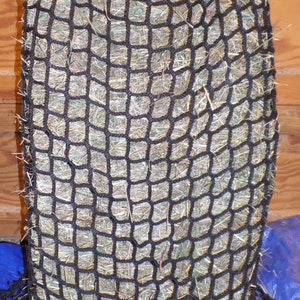 May include: A black hay net filled with hay. The net is made of a thick, durable material and has a drawstring closure.