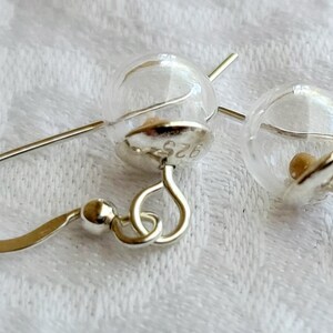 May include: A pair of dangle earrings featuring clear glass spheres attached to silver-toned metal caps. The metal caps are stamped with the text 925, indicating sterling silver composition. Each earring includes a curved silver-toned ear wire hook.