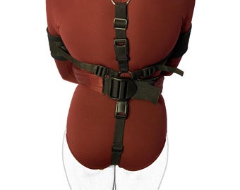 May include: Black restraint harness with adjustable straps and a metal ring. The harness is designed to secure the arms and wrists.