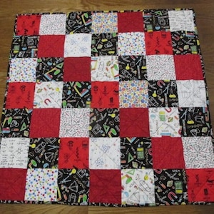 May include: A red and black patchwork quilt with a variety of science-themed fabric squares. The squares feature images of atoms, magnets, beakers, and the words "STEM", "MATH", and "SCIENCE".