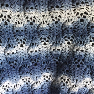 Könnte beinhalten: Ein handgefertigter, offen gewebter Häkelschal in Blau- und Weißtönen. Das komplizierte Muster erzeugt einen strukturierten, spitzenartigen Effekt. Der Farbverlauf geht von tiefem Blau zu helleren Farbtönen über.