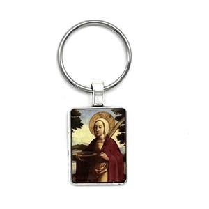 May include: A silver rectangular keyring featuring a religious painting. The painting shows a person with a halo, holding a bowl and staff, set against a landscape. The keyring has a silver ring.