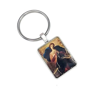 May include: A silver keychain with a rectangular charm featuring a colorful image of a woman holding a rope. The woman is wearing a blue and red dress and is surrounded by a gold background.