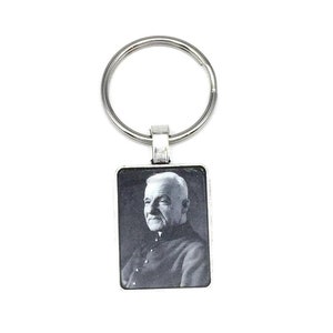 May include: A rectangular silver keyring featuring a black and white portrait of an elderly man. The portrait is framed in silver and connected to a circular key ring.