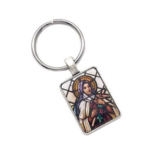 May include: Silver keychain with a rectangular charm featuring a stained glass image of a woman holding a rose. The woman is wearing a purple robe and a halo.