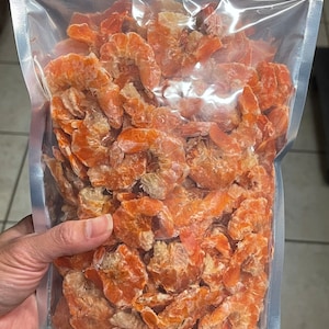 May include: A clear plastic bag filled with dried shrimp. The shrimp are a bright orange color and have a slightly crunchy texture.
