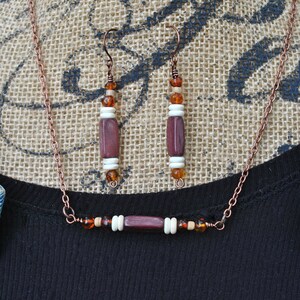 May include: A copper chain necklace with a wooden pendant and matching earrings. The necklace and earrings feature brown, white, and amber beads.