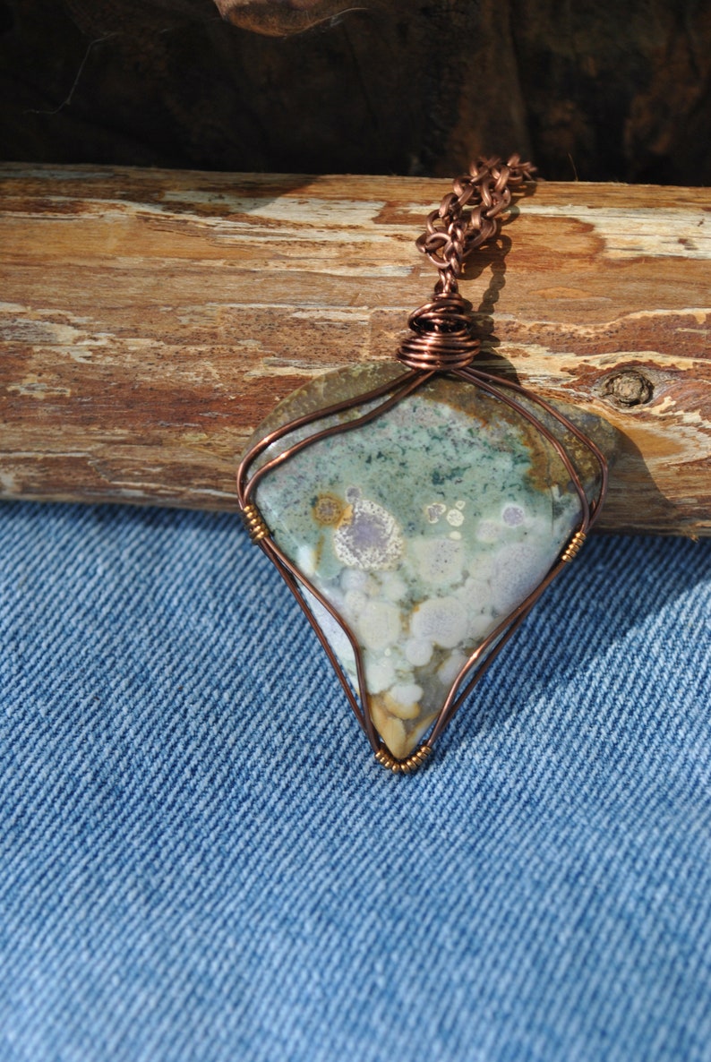 May include: A copper wire wrapped pendant featuring a green, white and brown agate stone with a unique pattern. The pendant is hanging from a copper chain.