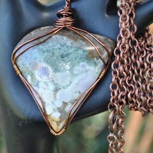 May include: A copper wire wrapped pendant featuring a green, brown, and white stone with a copper chain.