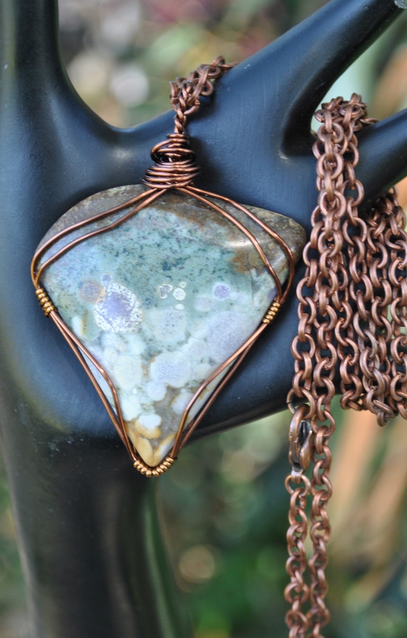 May include: A copper wire wrapped pendant featuring a green, brown, and white stone with a copper chain.