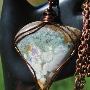 May include: A copper wire wrapped pendant featuring a green, white and brown agate stone with a copper chain.