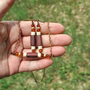 May include: A copper chain necklace with wooden and amber beads. The necklace has a matching pair of earrings with wooden and amber beads.