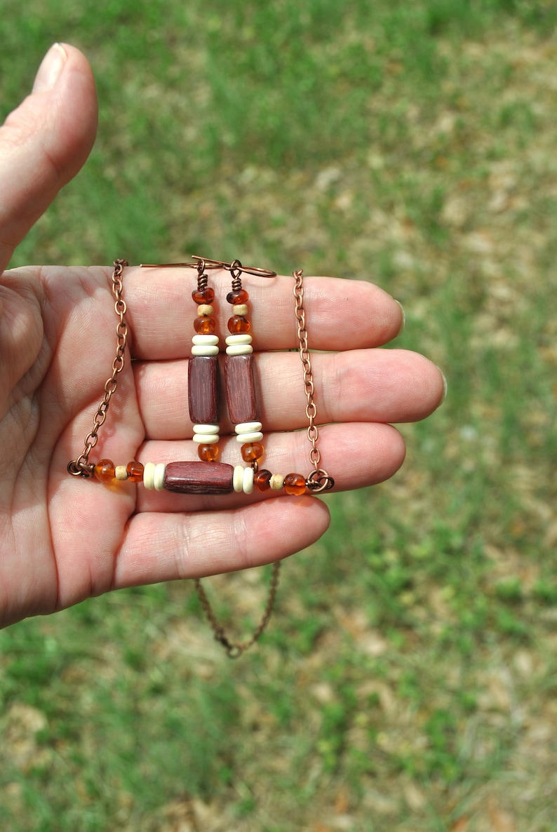 May include: A copper chain necklace with wooden and amber beads. The necklace has a matching pair of earrings with wooden and amber beads.