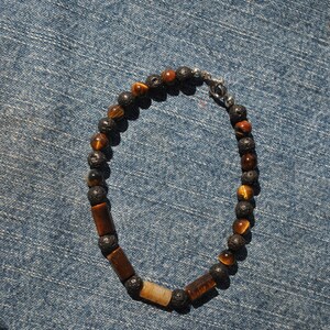 Puede incluir: Un brazalete con cuentas de ojo de tigre marr&oacute;n y cuentas de roca volc&aacute;nica negra. El brazalete tiene un cierre plateado.