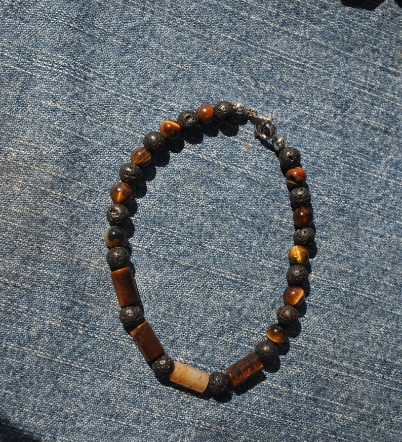 Puede incluir: Un brazalete con cuentas de ojo de tigre marr&oacute;n y cuentas de roca volc&aacute;nica negra. El brazalete tiene un cierre plateado.