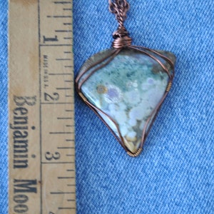 May include: A copper wire wrapped pendant featuring a light blue, green, and white agate stone. The pendant is approximately 5 cm in length and is hanging from a copper chain.