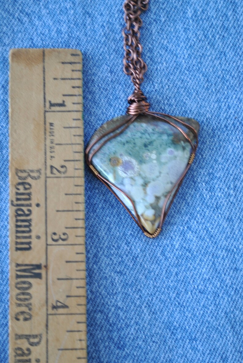 May include: A copper wire wrapped pendant featuring a light blue, green, and white agate stone. The pendant is approximately 5 cm in length and is hanging from a copper chain.
