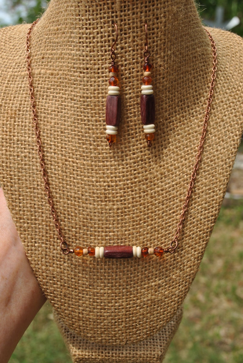 May include: A copper chain necklace with a wooden bead and amber-colored glass beads. Matching earrings with wooden beads and amber-colored glass beads.