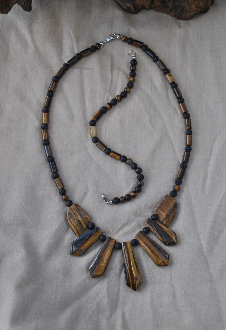 Puede incluir: Un collar de cuentas marrones y negras con un colgante de ojo de tigre. El colgante est&aacute; hecho de varias piezas largas y puntiagudas de piedra de ojo de tigre.