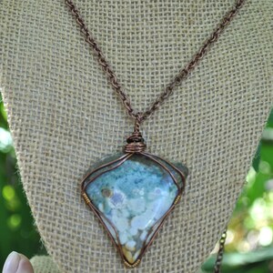 May include: A copper chain necklace with a triangular pendant featuring a light blue, white and brown agate stone wrapped in copper wire.