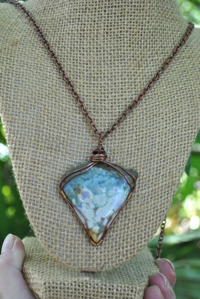 May include: A copper chain necklace with a triangular pendant featuring a light blue, white and brown agate stone wrapped in copper wire.