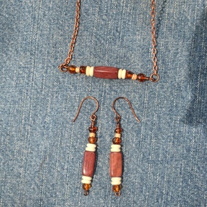 May include: A copper chain necklace with a wooden bead and amber beads. Matching earrings with wooden beads and amber beads.