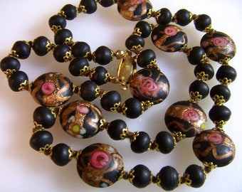 May include: A vintage necklace featuring matte black beads and larger, decorative beads with pink rose and gold accents. The necklace has a gold-tone clasp and connectors, showcasing a classic jewelry design.