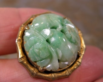 May include: A green jade carved floral design brooch set in a gold tone bamboo-style frame.