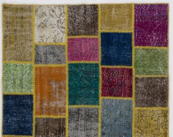 Puede incluir: Una alfombra de retazos con una variedad de parches rectangulares en tonos de verde, naranja, azul, rosa y marrón. Los parches están delineados con costuras amarillas. La alfombra tiene un aspecto envejecido y vintage.