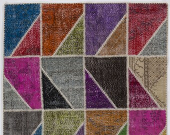 Puede incluir: Una alfombra de patchwork colorida con un patrón geométrico. La alfombra está hecha de diferentes telas y colores, incluyendo rosa, morado, azul, verde, marrón y beige. La alfombra tiene un aspecto desgastado y es perfecta para agregar un toque de estilo bohemio a cualquier habitación.