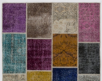 Puede incluir: Una alfombra de patchwork con una variedad de colores y patrones, incluyendo azul, verde, morado y amarillo. La alfombra está hecha de cuadrados más pequeños de tela que se han cosido juntos.