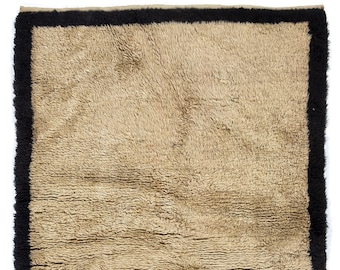 Può includere: Un tappeto shaggy beige con un bordo nero. Il tappeto ha una texture morbida e soffice.