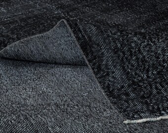 May include: A black and grey rug with a distressed, vintage look. The rug is folded in half, showing the underside of the fabric.