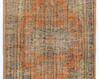 May include: A vintage rug with a faded orange background and intricate floral patterns in shades of beige, green, and purple. The rug has a distressed look with a worn border.
