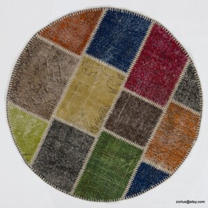 May include: Round patchwork rug with a variety of colors and textures, including brown, green, blue, red, and yellow. The rug is made of different pieces of fabric sewn together.