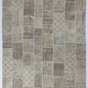 May include: A patchwork rug with a beige background and brown floral patterns. The rug is made of different pieces of fabric sewn together.