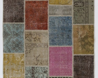 Puede incluir: Alfombra rectangular de patchwork con una variedad de colores y patrones. La alfombra está compuesta por numerosos parches rectangulares en tonos de rosa, verde, azul, marrón y amarillo. Algunos parches presentan diseños florales o geométricos. La alfombra tiene un aspecto envejecido.
