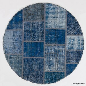 Puede incluir: Alfombra redonda de patchwork en tonos azules y grises. La alfombra está hecha de varios trozos de tela cosidos juntos para crear un diseño único.