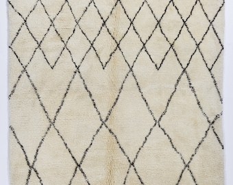 May include: A white Moroccan rug with a black diamond pattern. The rug has a soft, fluffy texture and is made of wool.