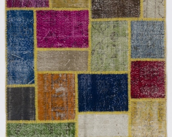 Puede incluir: Una alfombra de patchwork con una variedad de colores y patrones, incluyendo azul, verde, rojo, morado y marrón. La alfombra está hecha de diferentes piezas de tela que se han cosido juntas.
