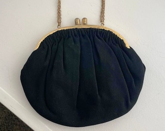 Könnte beinhalten: Eine schwarze Stoff-Clutch mit einer goldenen Kettenkette und einem goldenen Verschluss.