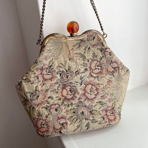 May include: A vintage floral tapestry clutch bag with a gold chain strap and a brown plastic top closure.