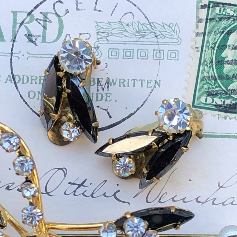 Puede incluir: Un par de pendientes vintage de clip con piedras negras en forma de marquesa y brillantes transparentes. Los pendientes son de color dorado y tienen un dise&ntilde;o cl&aacute;sico.