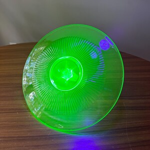 Może przedstawiać: Żywy, zielony szklany talerz z centralnym wzorem w kształcie gwiazdy i promieniowymi rowkami. Talerz ma okrągły kształt i wydaje się być wykonany z przezroczystego materiału. Kolor jest jasny, prawie neonowy.