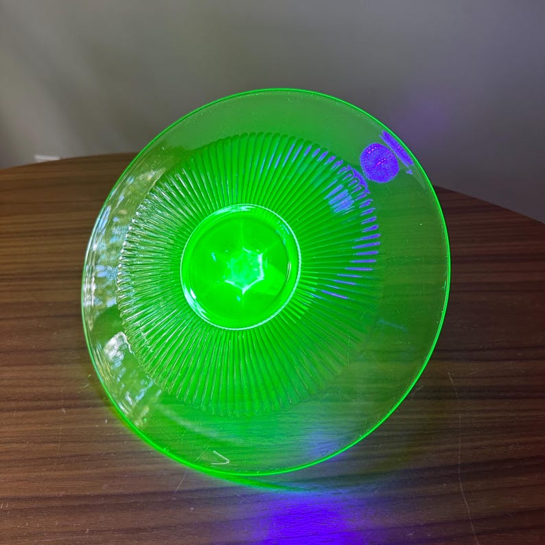 Może przedstawiać: Żywy, zielony szklany talerz z centralnym wzorem w kształcie gwiazdy i promieniowymi rowkami. Talerz ma okrągły kształt i wydaje się być wykonany z przezroczystego materiału. Kolor jest jasny, prawie neonowy.