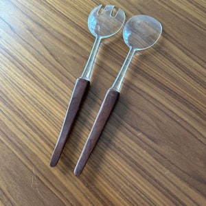 May include: A set of two clear glass salad servers with brown wooden handles.