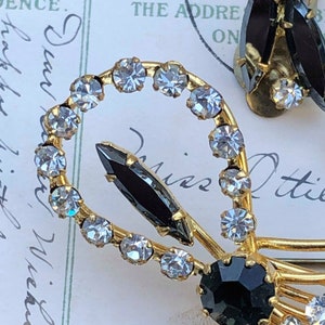 Puede incluir: Un par de pendientes de tono dorado con diamantes de imitaci&oacute;n negros y transparentes. Los pendientes tienen forma de lazo con un solo diamante de imitaci&oacute;n negro en el centro del lazo.